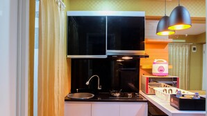 Une cuisine compacte avec un poêle noir, un évier et un four à micro-ondes. Deux lampes suspendues sont fixées au-dessus du plan de travail.