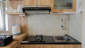A modern kitchen with wooden cabinets, a stainless steel sink, a gas stove, and a coffee maker. - Best Furnished 2BR Mall Access at Green Pramuka Apartment (Jakarta)