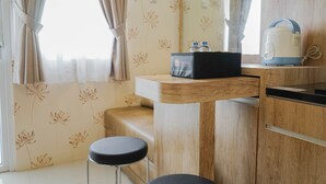 A compact kitchenette with a wooden countertop, a kettle, and a small table with two bottles. - Best Furnished 2BR Mall Access at Green Pramuka Apartment (Jakarta)