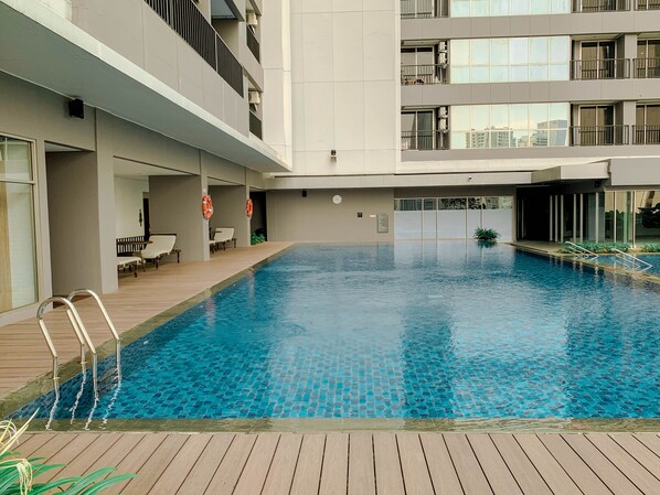 A modern indoor swimming pool with a wooden deck, built-in seating, and a view of the surrounding building. - Great Location Studio at The Newton Ciputra World 2 Apartment (Jakarta)