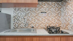 A kitchen with a stainless steel sink, a gas stove, and a tiled backsplash. - Best Homey Elegant Studio Room at Amethyst Apartment (Jakarta)