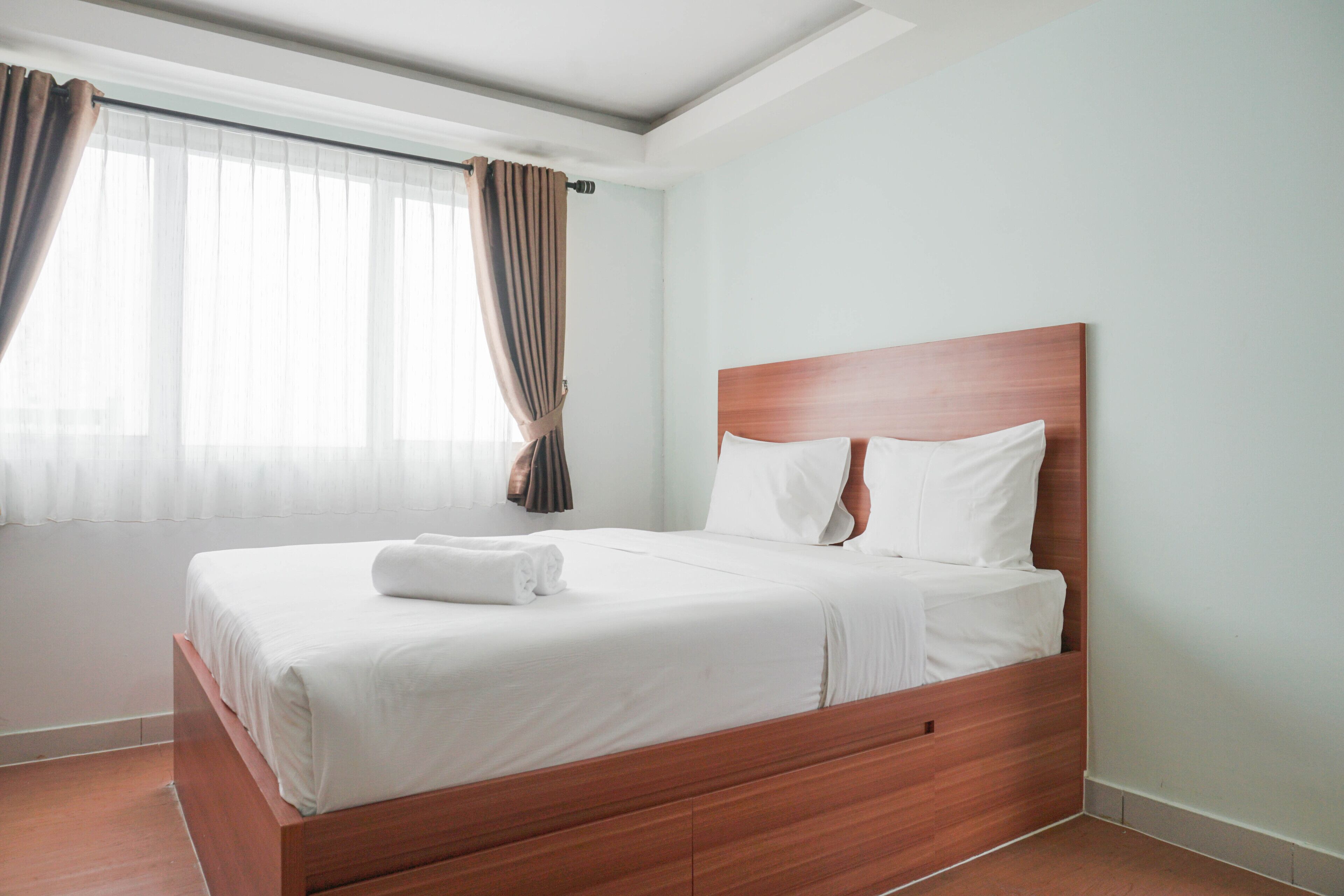 A neatly made bed with white linens and a wooden headboard in a hotel room.