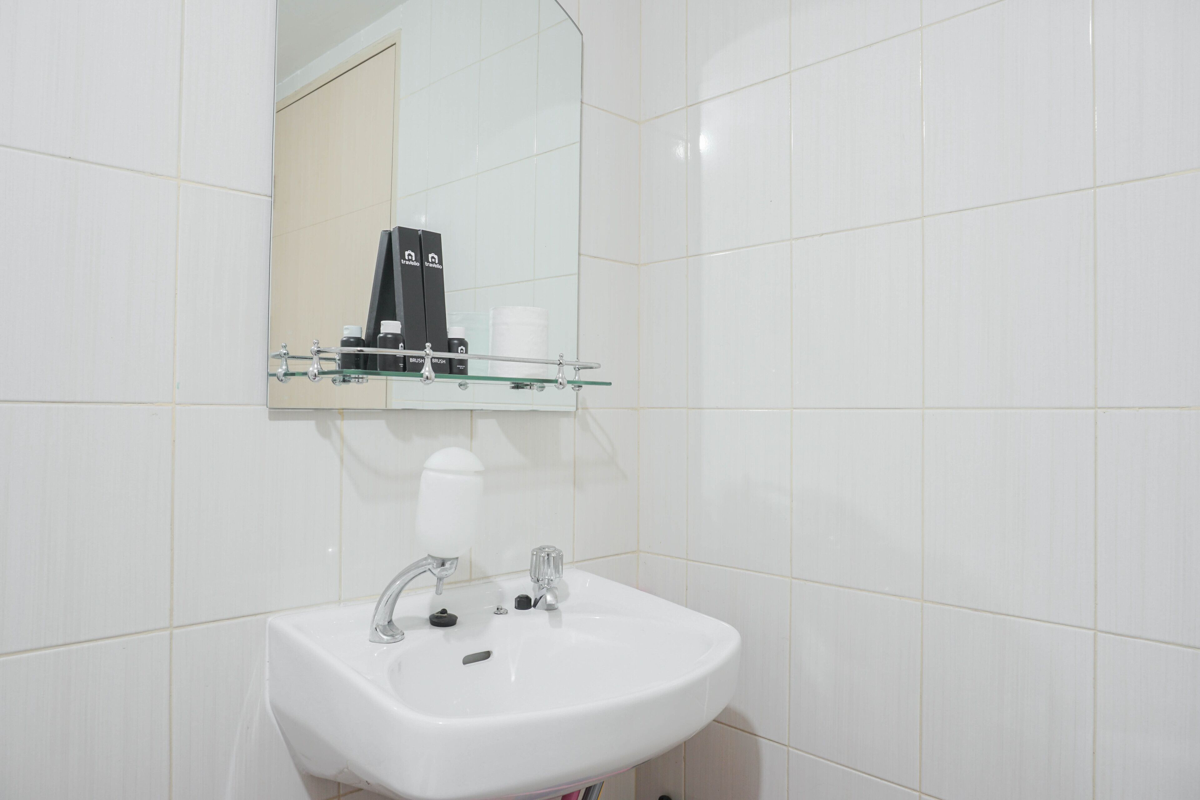 A bathroom with a white sink, a mirror, and a shelf with toiletries.