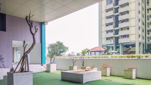 An outdoor area with concrete planters, a green artificial turf surface, and a modern building in the background. - Best Homey Elegant Studio Room at Amethyst Apartment (Jakarta)