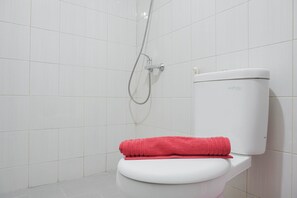 A white toilet with a red towel on top, a showerhead, and a white tiled wall. - Best Homey Elegant Studio Room at Amethyst Apartment (Jakarta)