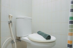 A toilet with a green towel on it, a shower hose, and a tiled wall. - Cozy Studio at Amethyst Apartment (Jakarta)
