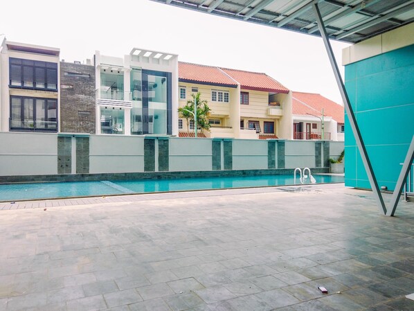 A swimming pool area with a modern building in the background. - Cozy Studio at Amethyst Apartment (Jakarta)