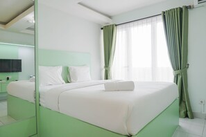 A neatly made bed with white linens, a green headboard, and a green curtain on a window. - Cozy Studio at Amethyst Apartment (Jakarta)