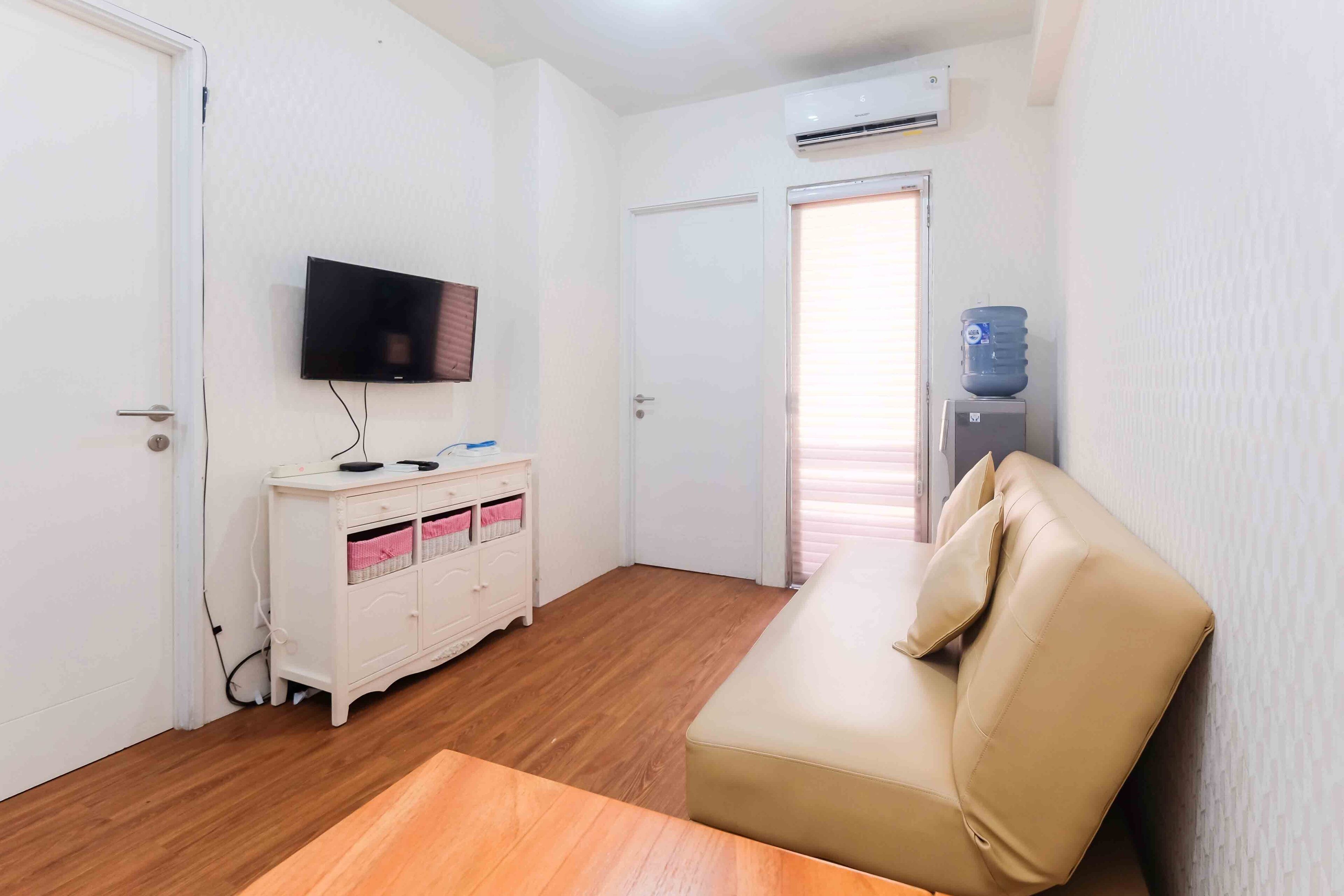 A room with a beige sofa, a white cabinet, a flat-screen TV, and an air conditioning unit.