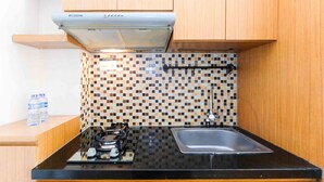 A compact kitchen with a black countertop, a gas stove, a stainless steel sink, and a Modena range hood. - Homey and Cozy Living Studio at Pakubuwono Terrace Apartment (Jakarta)