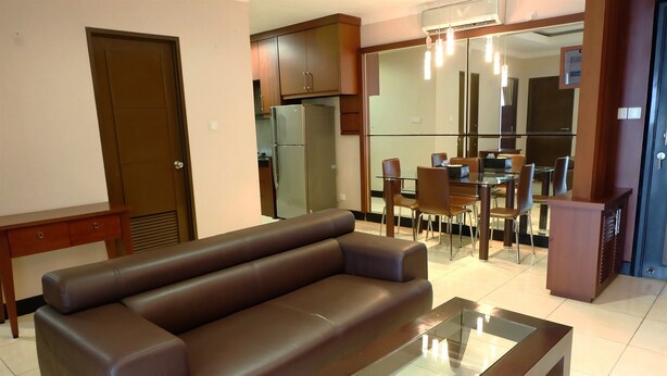 A modern living room with a brown leather sofa, a glass-top coffee table, and a dining area with a glass table and chairs. - 2BR Prestige Dharmawangsa Essence Apartment Suites (Jakarta)