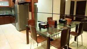 A modern kitchen with a glass dining table, brown chairs, and a stainless steel refrigerator. - 2BR Prestige Dharmawangsa Essence Apartment Suites (Jakarta)
