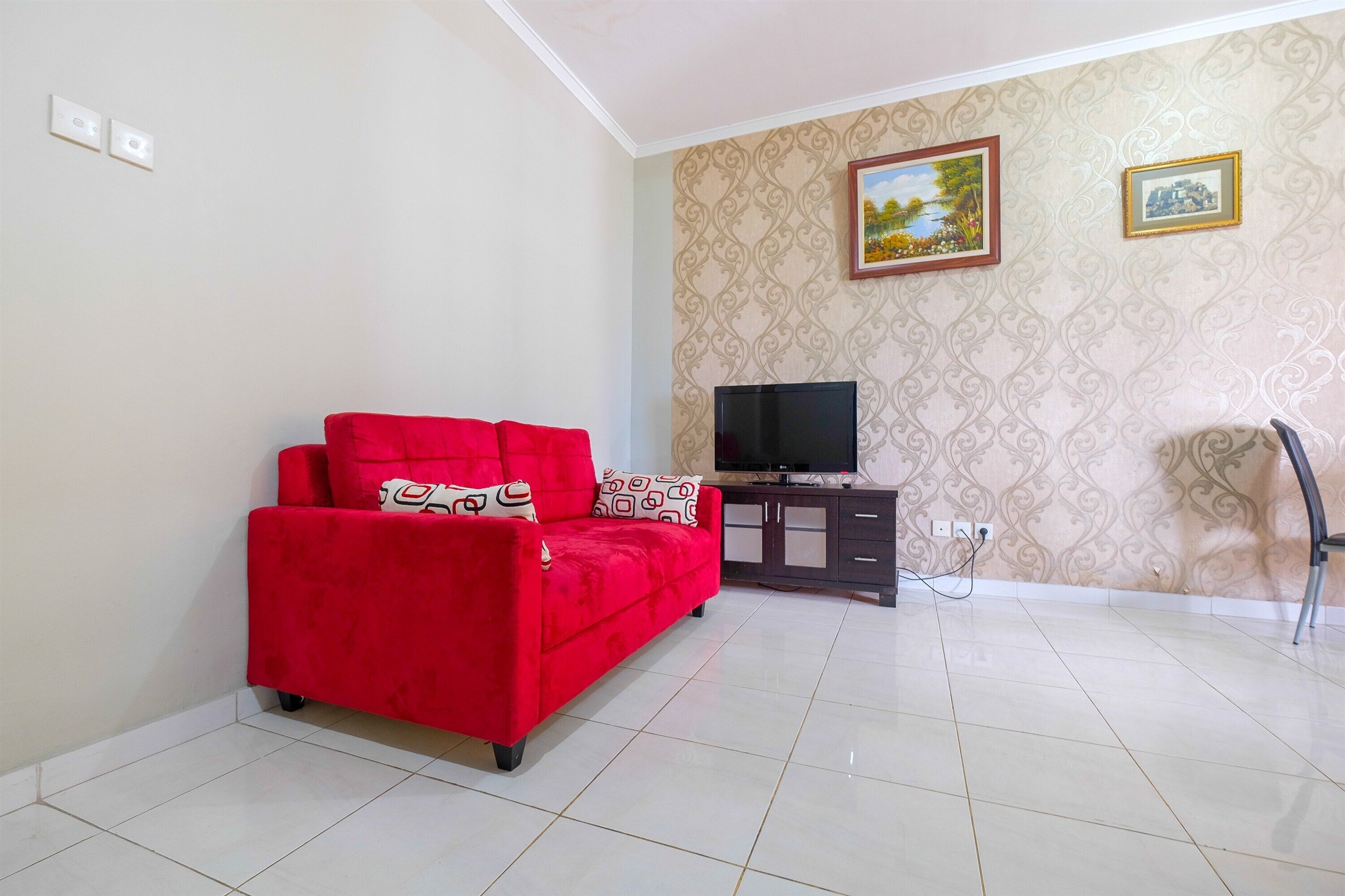 A living room with a red sofa, a TV on a stand, and patterned wallpaper.
