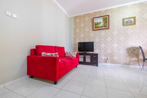 A living room with a red sofa, a TV on a stand, and patterned wallpaper.