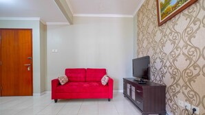 A living room with a red sofa, a dark wooden cabinet, and a television. - Strategic 2BR at Sudirman Park Apartment (Jakarta)