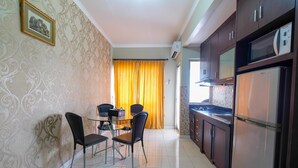 A compact kitchen with a refrigerator, microwave, and a dining area with chairs and a table. - Strategic 2BR at Sudirman Park Apartment (Jakarta)