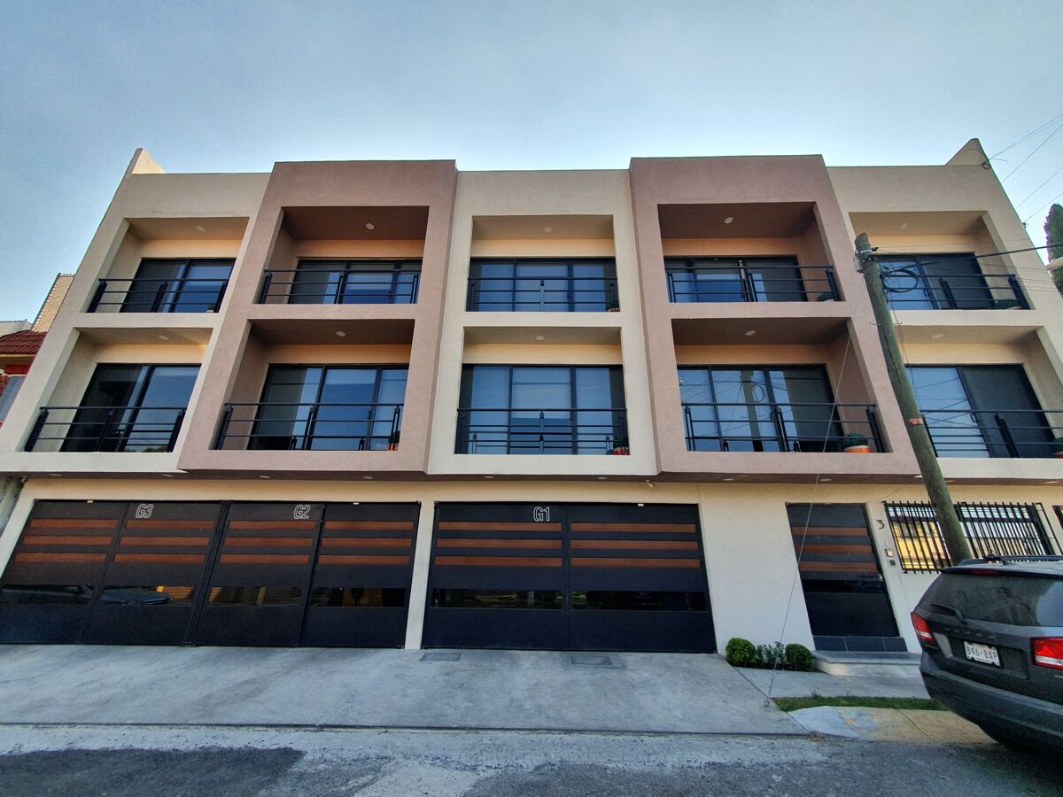 Un immeuble à plusieurs étages doté d’une architecture moderne, caractérisé par un toit plat, de grandes fenêtres et une série de portes de garage au niveau du rez-de-chaussée.