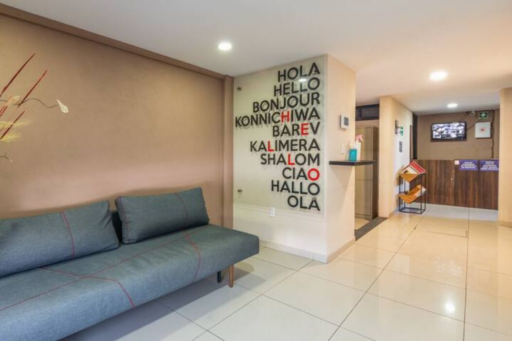 A reception area with a sofa, a wall with multilingual greeting signs, a reception desk, and a television screen.