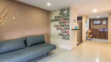 A reception area with a sofa, a wall with multilingual greeting signs, a reception desk, and a television screen.