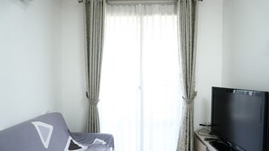 A room with a bed, a television on a stand, and a window with curtains. - Wonderful 2BR Apartment at Belmont Residence Puri (Jakarta)