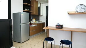 A compact kitchen with a refrigerator, wooden cabinets, a sink, and a clock on the wall. - Wonderful 2BR Apartment at Belmont Residence Puri (Jakarta)