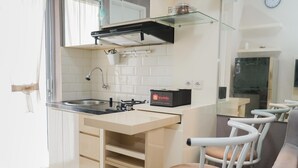 A compact kitchen with a sink, stove, and a glass shelf. There is a chair and a small table in the dining area. - Stunning 2BR at Bassura City Cipinang Apartment (Jakarta)