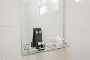 Ein Badezimmer mit einer Glasablage für Toilettenartikel, einem Handtuchhalter und einem Spiegel.