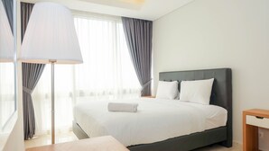 A hotel room with a large bed, a bedside table, a lamp, and a view of the outside through the window. - Posh 2BR at The Empyreal Condominium Epicentrum Apartment (Jakarta)