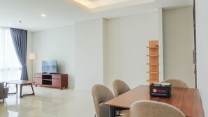 A modern hotel room with a dining table, chairs, a TV, and a wooden shelf. - Posh 2BR at The Empyreal Condominium Epicentrum Apartment (Jakarta)