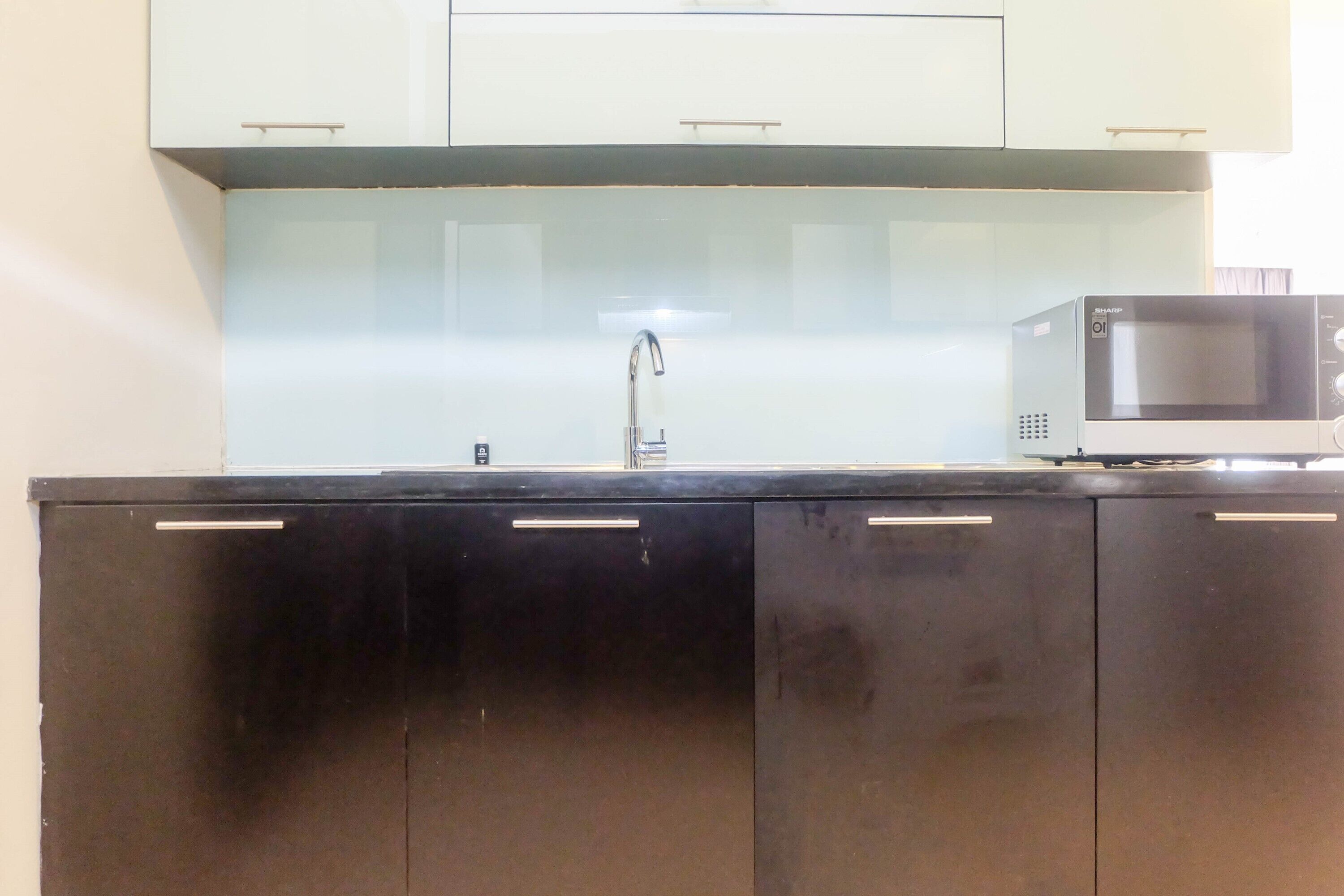 A kitchen with a black countertop, a stainless steel sink, and a microwave.