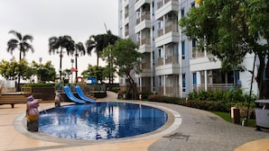 A swimming pool with a slide, surrounded by palm trees and a multi-story building with balconies. - Modern Studio Apartment at Tanglin Tower Supermall Mansion (Surabaya)