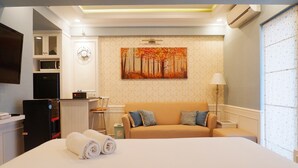 A hotel room with a bed, a sofa, a painting of a forest, a clock, and a TV on the wall. - Modern Studio Apartment at Tanglin Tower Supermall Mansion (Surabaya)