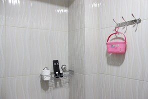 Casa de banho com azulejos brancos, uma prateleira de metal com ganchos, uma cesta cor-de-rosa e uma estante de metal com produtos de higiene pessoal.