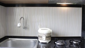 A kitchen with a stainless steel sink, a white and brown patterned rice cooker, and a black stove with two burners. - Minimalist Studio Gateway Ahmad Yani (Bandung)
