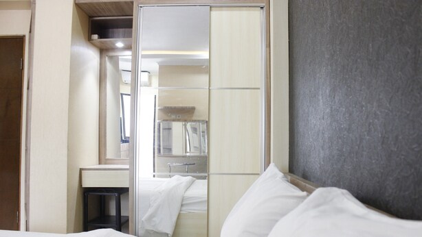 A hotel room with a bed, a mirror, a wardrobe, and a sink. - Minimalist Studio Gateway Ahmad Yani (Bandung)