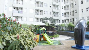A playground with a slide and climbing structures, surrounded by greenery and a modern building with balconies. - Cozy 2BR Apartment at Parahyangan Residence Bandung near UNPAR (Bandung)