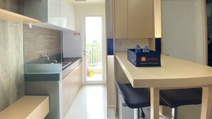 A compact kitchen with modern appliances, a small dining area, and a view of the outside balcony. - Cozy 2BR Apartment at Parahyangan Residence Bandung near UNPAR (Bandung)