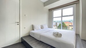 A modern bedroom with a bed, a window with a city view, and a door. - Cozy 2BR Apartment at Parahyangan Residence Bandung near UNPAR (Bandung)