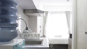 A modern hotel room with a kitchen area, a large water dispenser, and a bed with a white comforter. - Modern Look Studio Apartment at Grand Asia Afrika (Bandung)