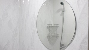 A bathroom with a large oval mirror, a shower with a handheld showerhead, and a towel rack. - Modern Look Studio Apartment at Grand Asia Afrika (Bandung)