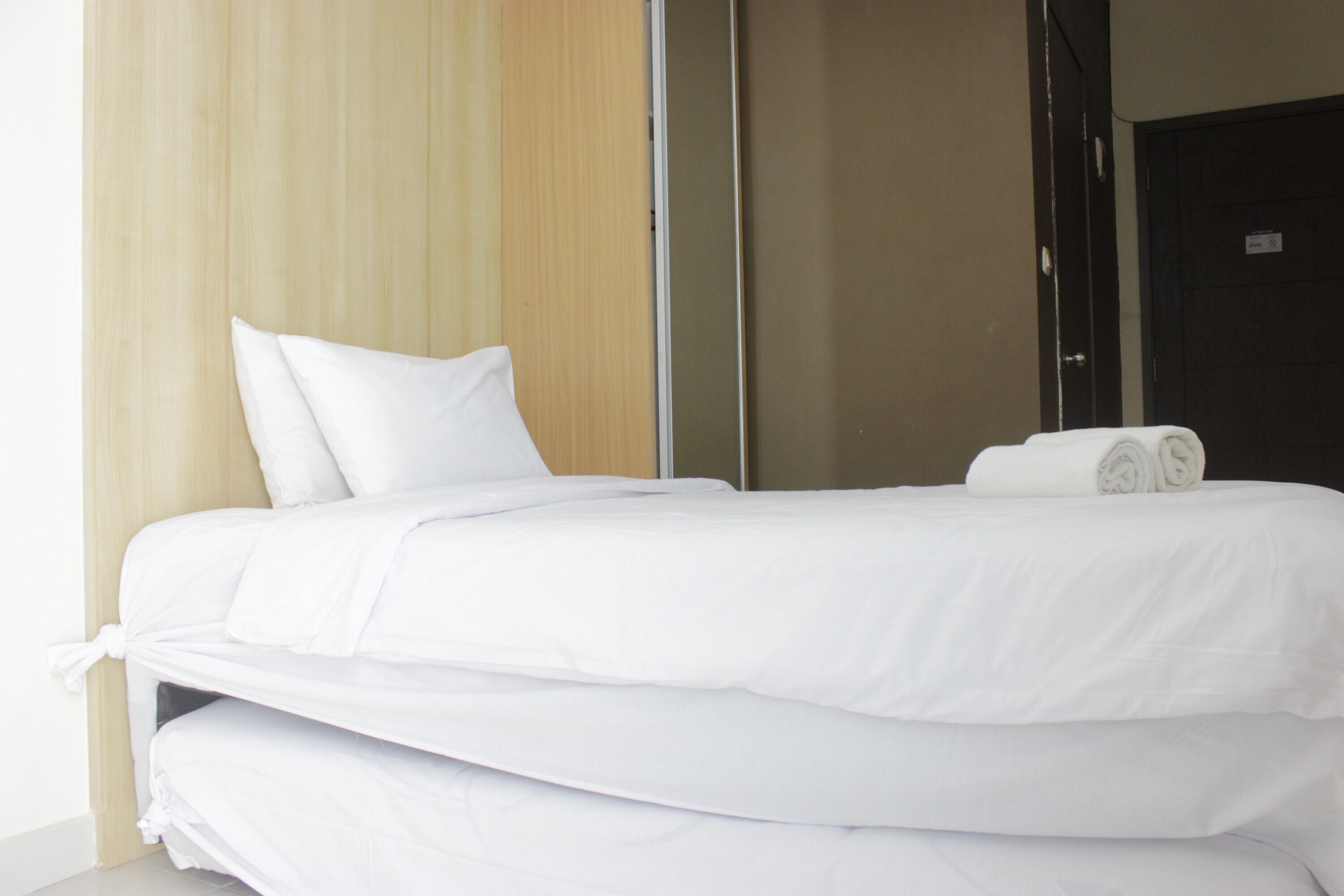 A neatly made bed with white linens and a rolled towel on top.
