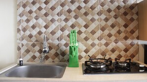 A kitchen with a sink, green-handled scissors, and a gas stove. - Appropriate Studio Apartment at Harvard Jatinangor near IPDN (Cileunyi)