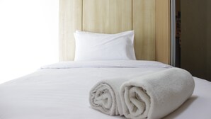 A neatly made bed with white linens and a rolled towel, set against a wooden panel wall. - Appropriate Studio Apartment at Harvard Jatinangor near IPDN (Cileunyi)