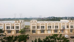 Una hilera de edificios de varios pisos en tonos beige con techos planos, probablemente residenciales u oficinas, con vista a una masa de agua y líneas de electricidad a lo lejos.