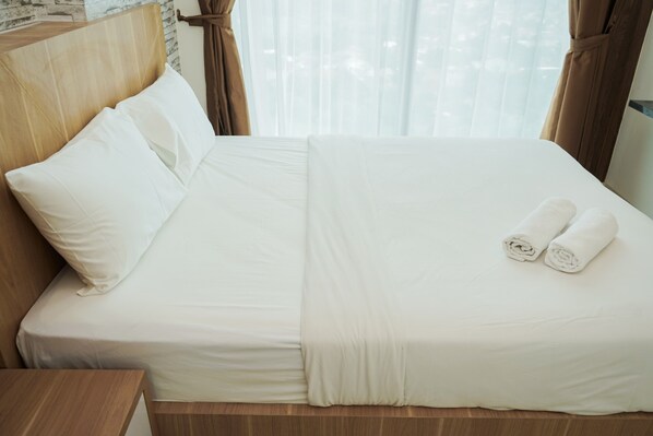Una cama bien hecha con sábanas blancas y dos toallas enrolladas encima.