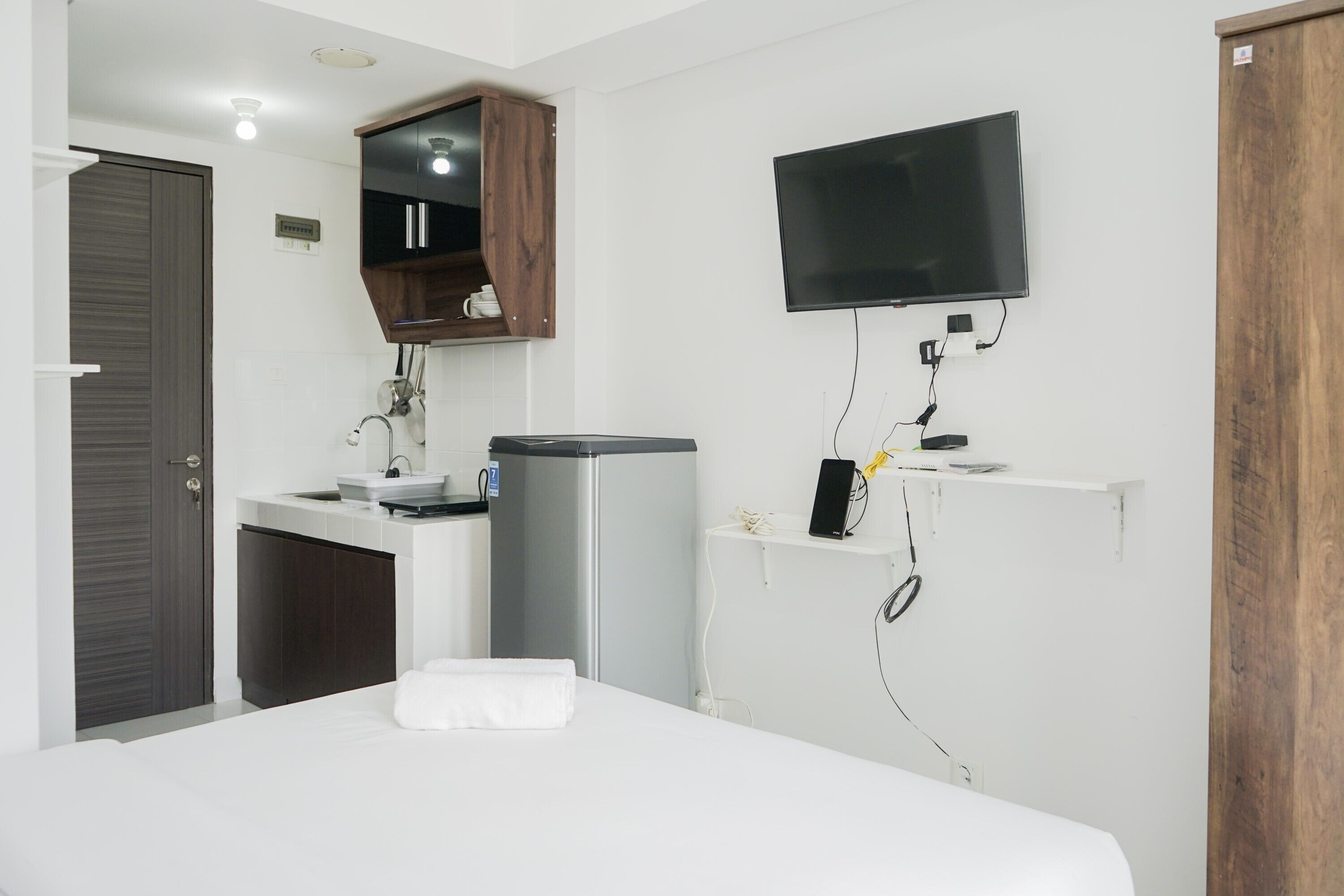A modern hotel room with a bed, a built-in sink, a mirror, a television mounted on the wall, and a wardrobe.