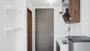 A modern bathroom with a wooden door, white walls, and a built-in sink. - Cozy Studio at Amazana Serpong Apartment (South Tangerang)