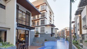 A modern residential building with a swimming pool, balconies, and a patio area with outdoor furniture. - Comfortable and Best Choice 1BR at Asatti Apartment (Pagedangan)