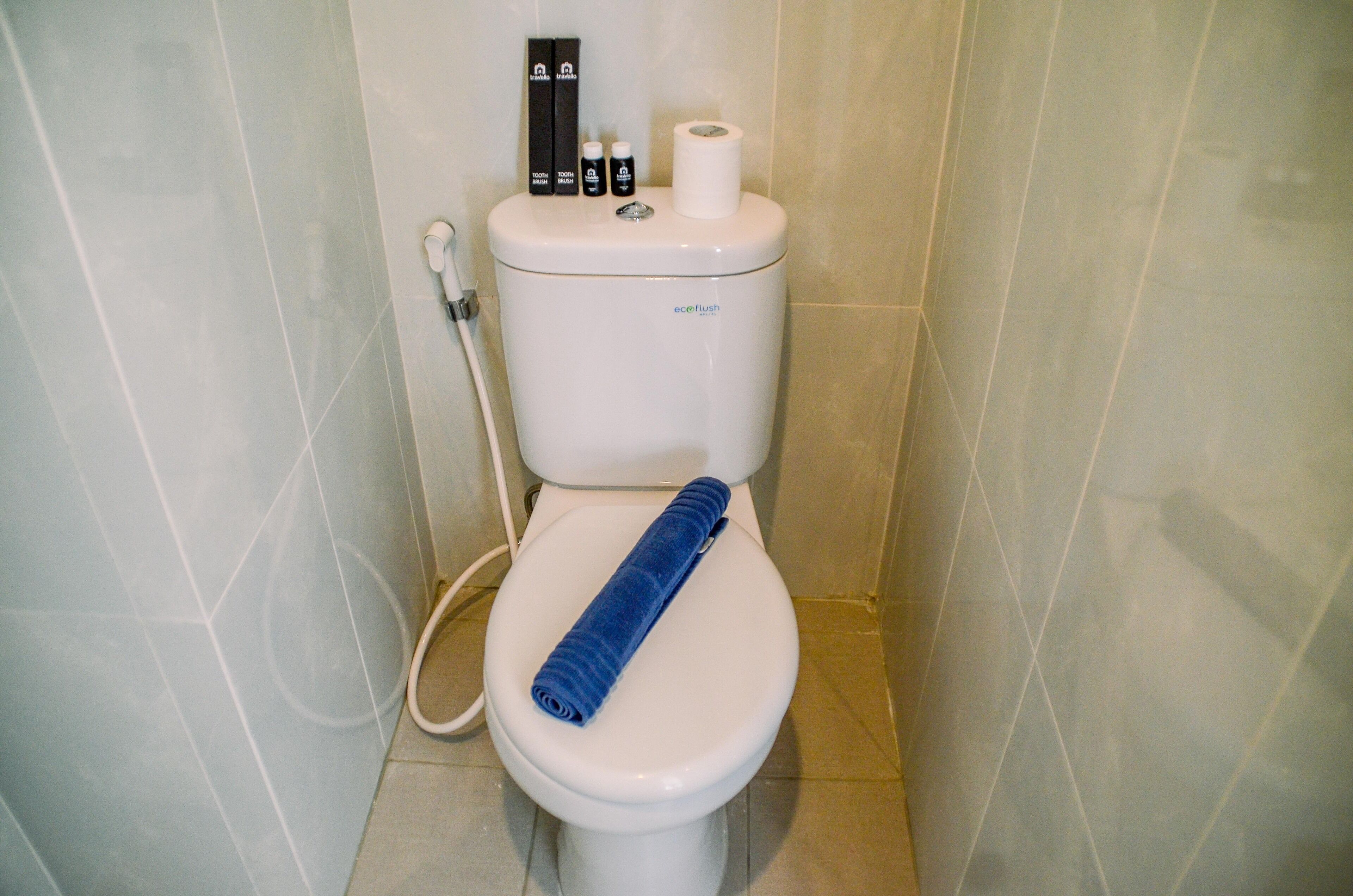 Sanitário com uma toalha azul no assento, um rolo de papel higiénico e duas garrafas no reservatório.
