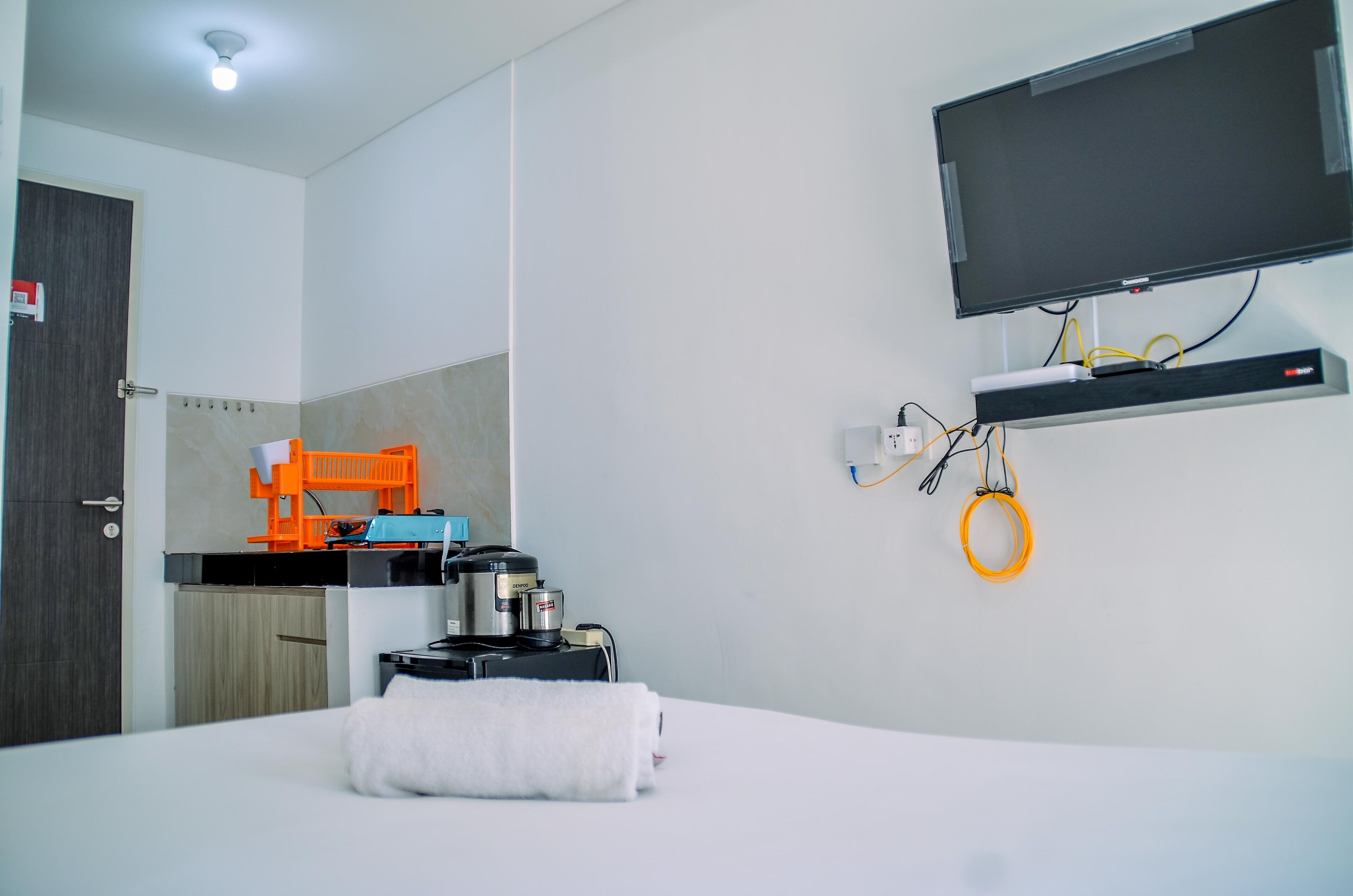 A hotel room with a bed, a TV mounted on the wall, a coffee machine, and a small orange chair.